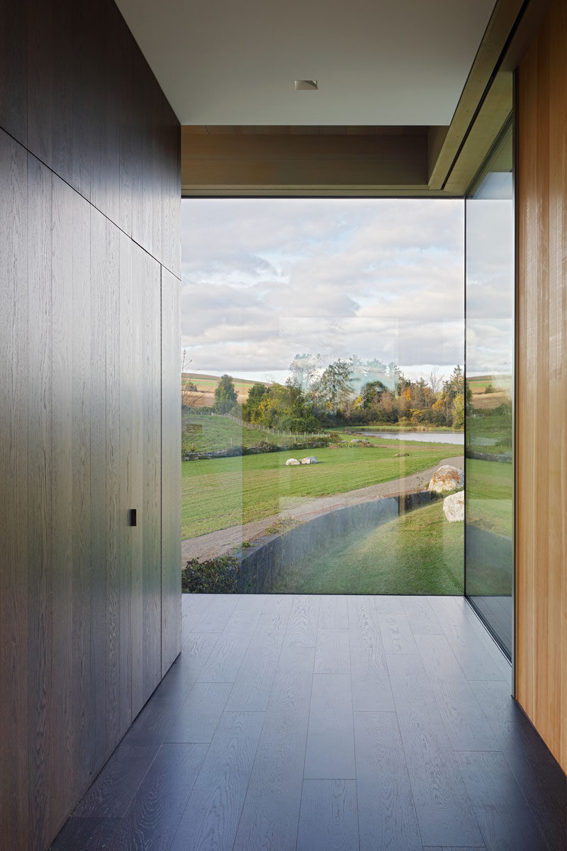 Inside this modern house, a dark wood wall with a hidden closet guides visitors to walk towards the windows, perfectly framing the view. #Windows #Entryway