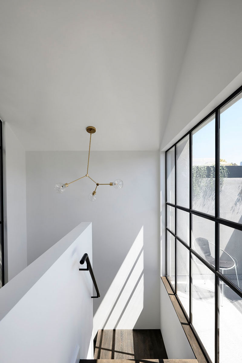 This minimalist stairwell features high ceilings and windows that look out onto a small outdoor space, that's accessed by some doors at the top of the stairs. #Windows