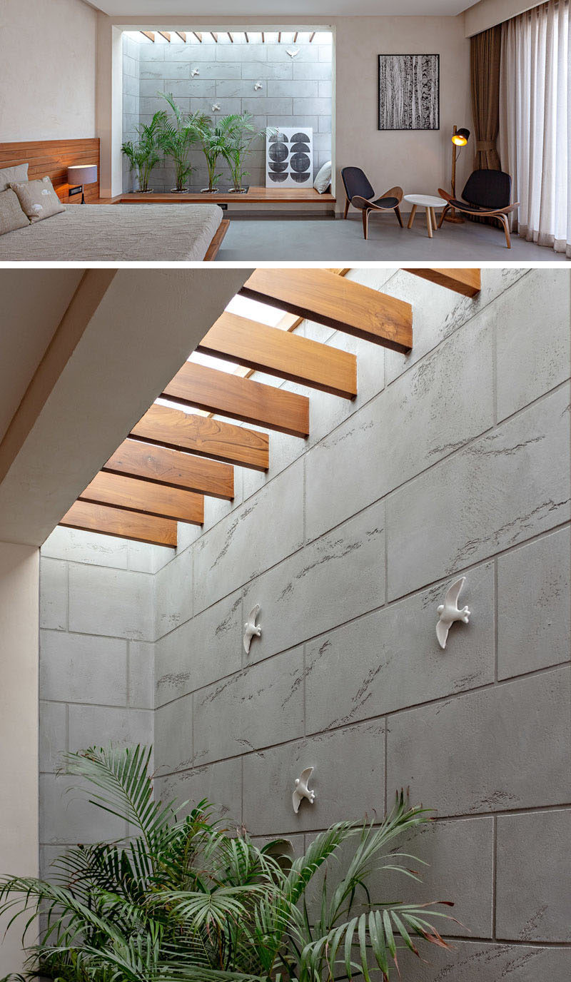 In this modern master bedroom, there's an opening displaying plants and a wood seating area, while a skylight provides additional light. #MasterBedroom #BedroomDesign