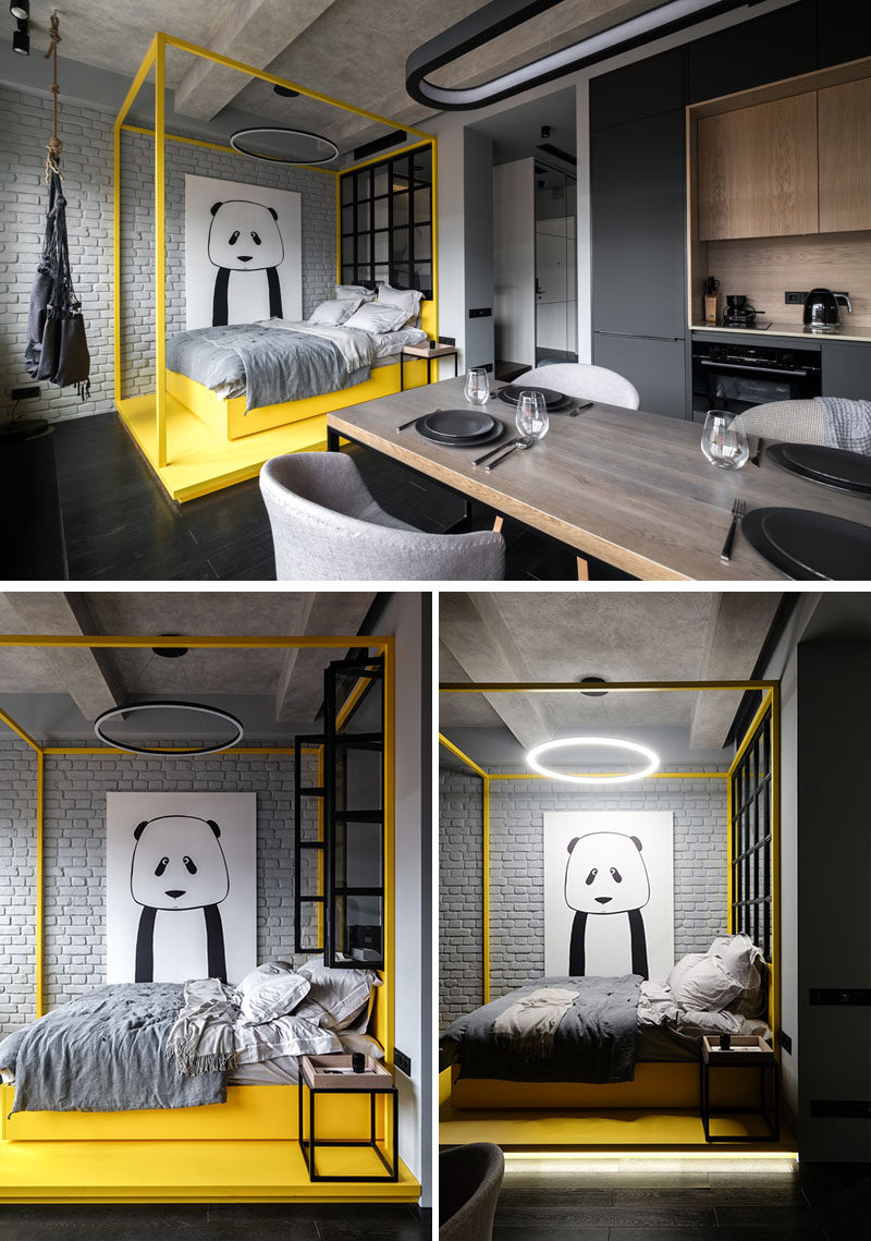 In this modern apartment, a bright yellow pop of color has been added to the monochrome interior in the form of a bed platform and bed frame. The bed sits beside a painted grey brick wall that has a large panda art piece, adding a bit of personality to the space.