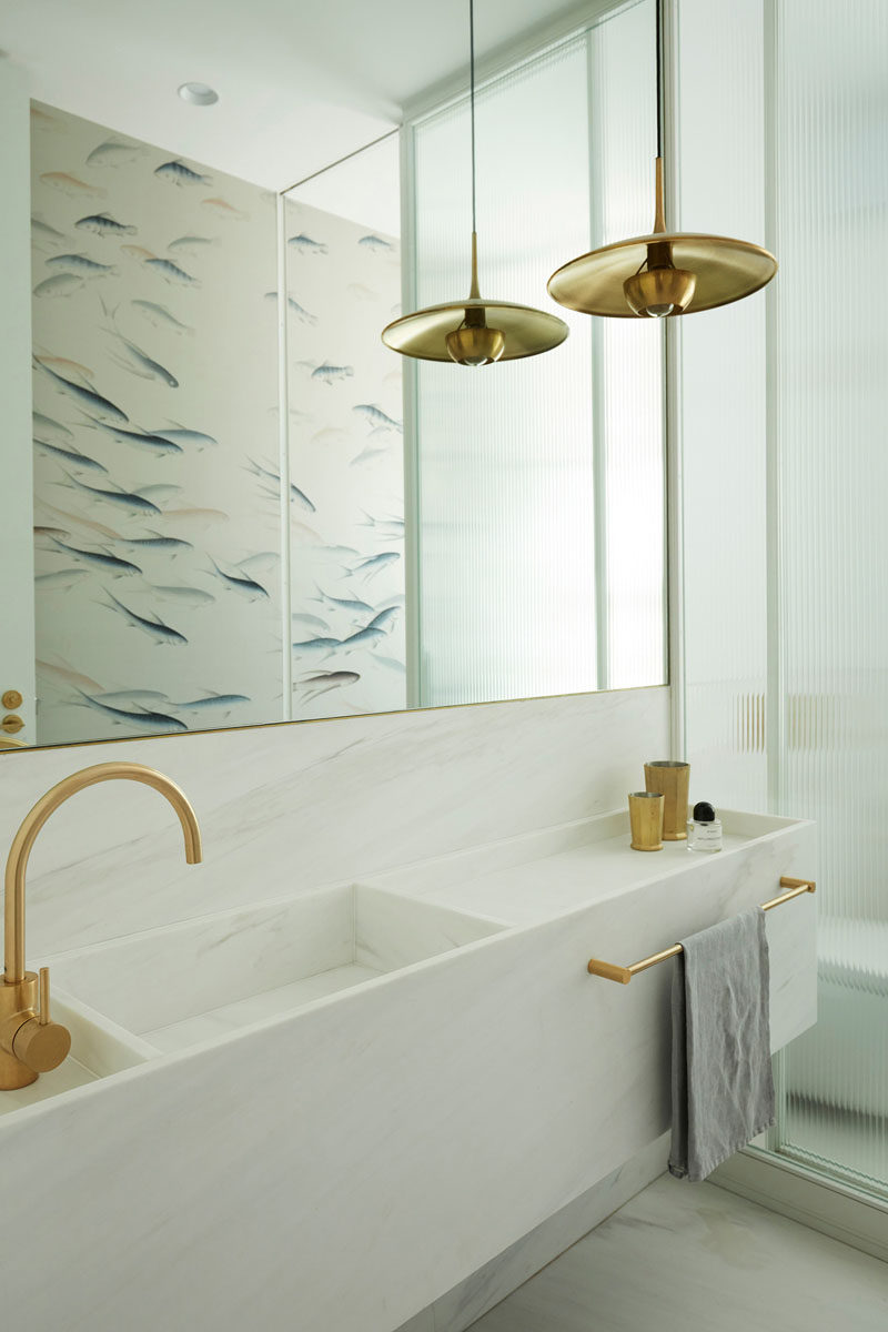 In this modern bathroom, a white vanity with a built-in basin sits below a large mirror that reflects the fish pattern on the opposite wall. #ModernBathroom #WhiteBathroom