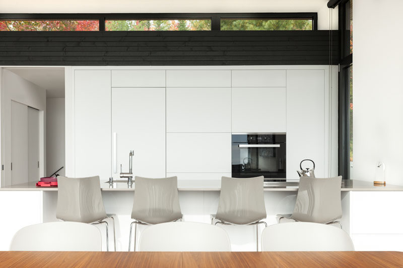 In this modern kitchen, white minimalist cabinets blend in seamlessly with the white walls, and contrast the dark wood accents. #ModernWhiteKitchen #WhiteKitchen #KitchenDesign