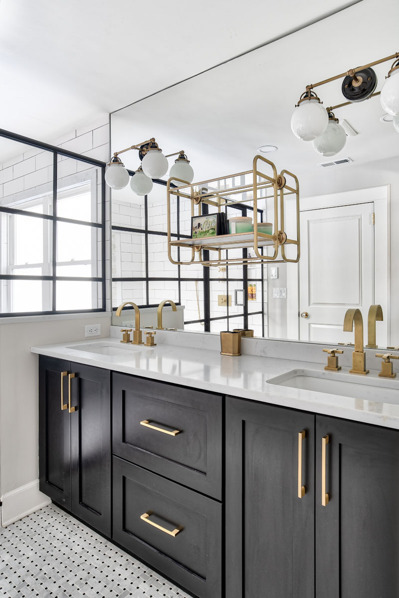 This modern bathroom features a dark vanity with dual undermount sinks, basketweave tile flooring, and a large mirror with a mounted shelf and sconces. #ModernBathroom #BathroomVanity #BathroomDesign