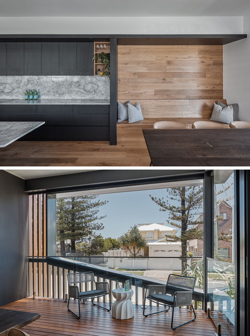 The black cabinetry of a modern kitchen meets a custom-designed built-in wood bench. The dining area opens up to an alfresco dining space with views of the street. #ModernInterior #BuiltInSeating #BlackCabinetry