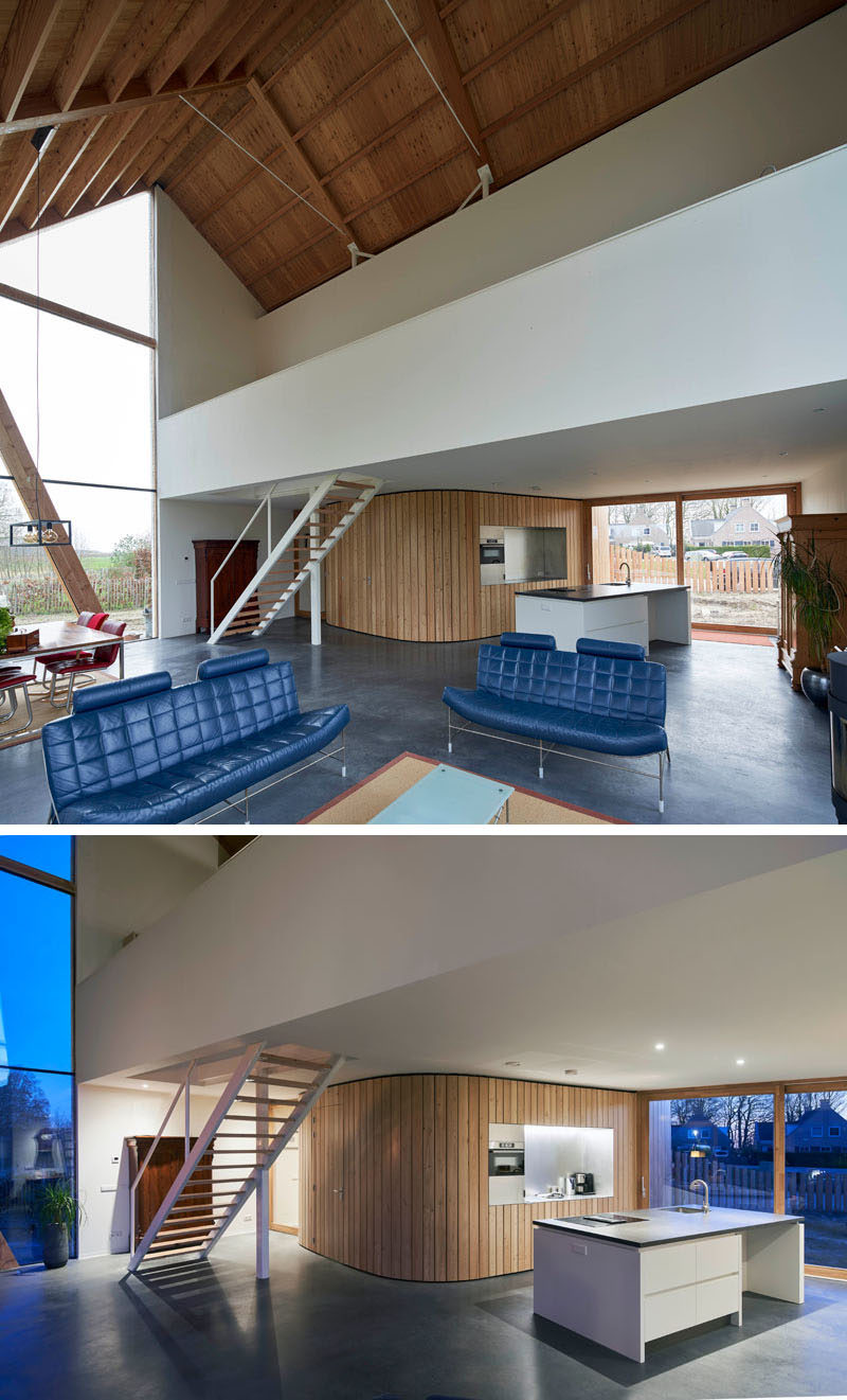 In this modern barn house, a curved wood wall flows from the front door and around to the kitchen. It also hides the laundry-room, toilet, cloak-room, and storage. #CurvedWoodWall #KitchenDesign