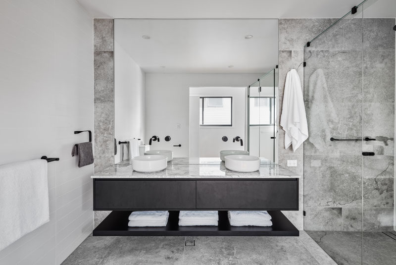 A simple color palette of grey, white, and black has been used in this modern bathroom, while a large mirror reflects the light from the window. #ModernBathroom #BathroomDesign