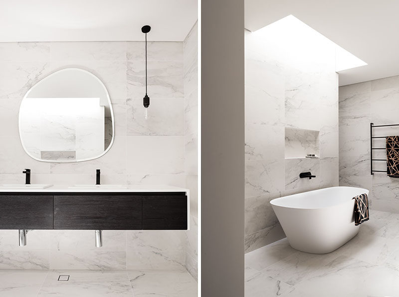 In this modern bathroom, a dark wood vanity contrasts the lightly colored tiled walls, while a freestanding bathtub is positioned beneath a skylight. #ModernBathroom #BathroomDesign