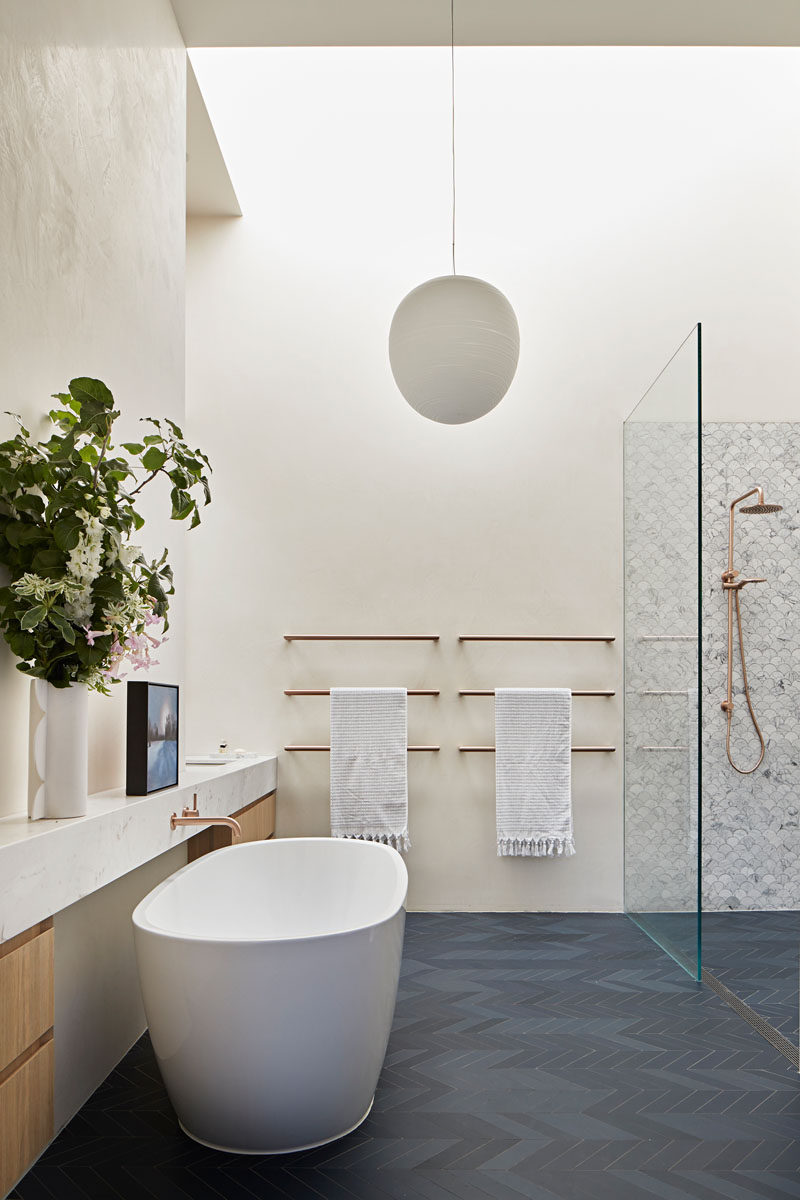 In this modern bathroom, dark grey chevron patterned floors contrast the white walls, while a freestanding bathtub sits opposite the shower. #ModernBathroom #BathroomDesign