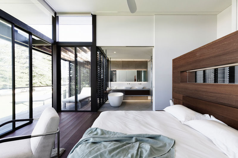 In this modern master bedroom, a rich wood accent wall complements the wood flooring, while the open ensuite bathroom has the bath positioned for views of the water. #MasterBedroom #OpenEnsuite #Bathroom