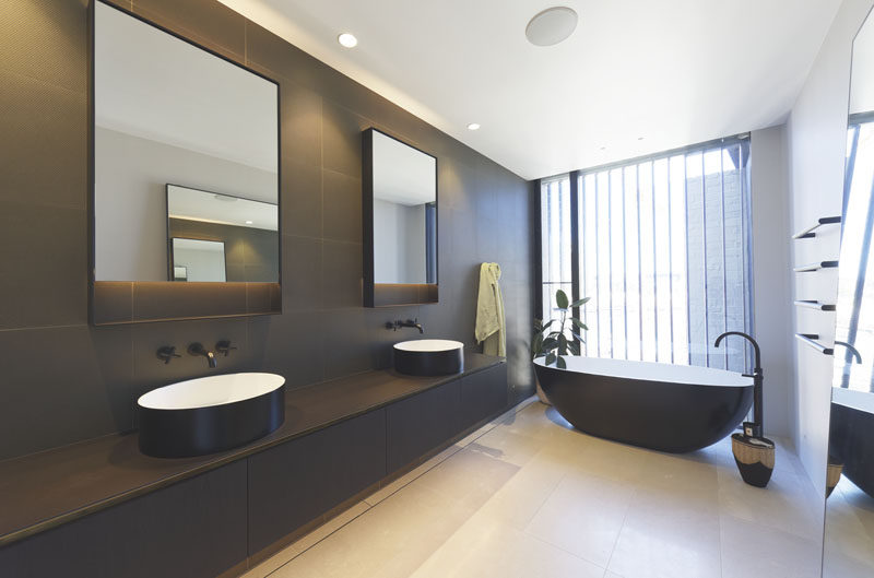 In this modern bathroom, a contrasting color palette has been used, with the exterior of the bathtub complementing the dark grey wall tiles and a dark vanity, while the floor and ceiling has been kept light. #ModernBathroom #BathroomDesign