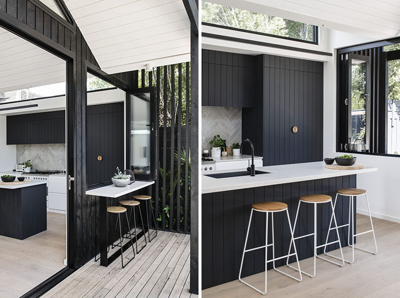 Large sliding doors and folding windows connect the new interior spaces, like the kitchen, living room, and dining room with the backyard. #BlackSiding #ModernKitchen #Bar #BlackKitchen