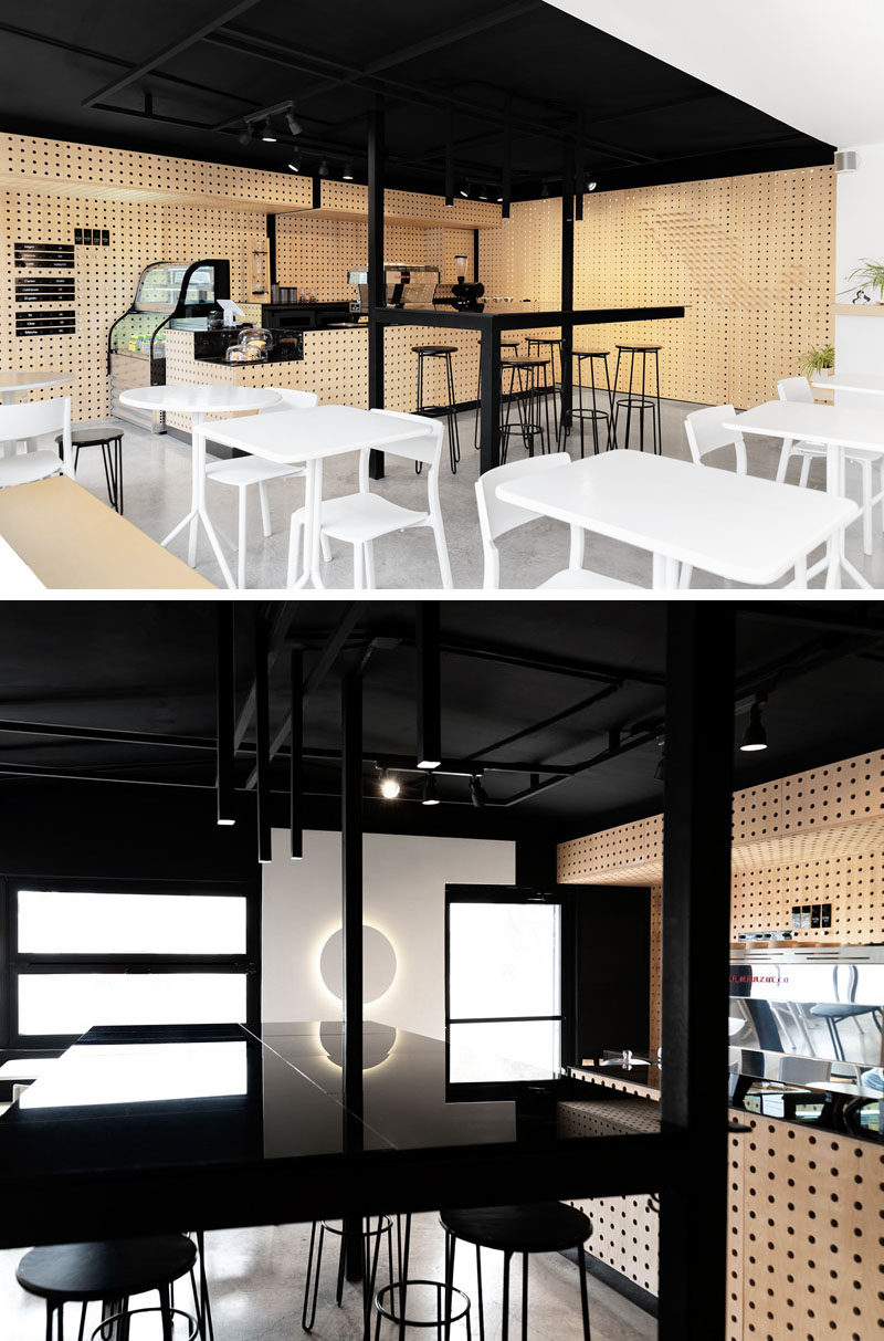 This modern coffee shop interior combines perforated wood walls with a black ceiling and accents, concrete flooring, and white furniture and walls. #CoffeeShop #CafeDesign #Interiors