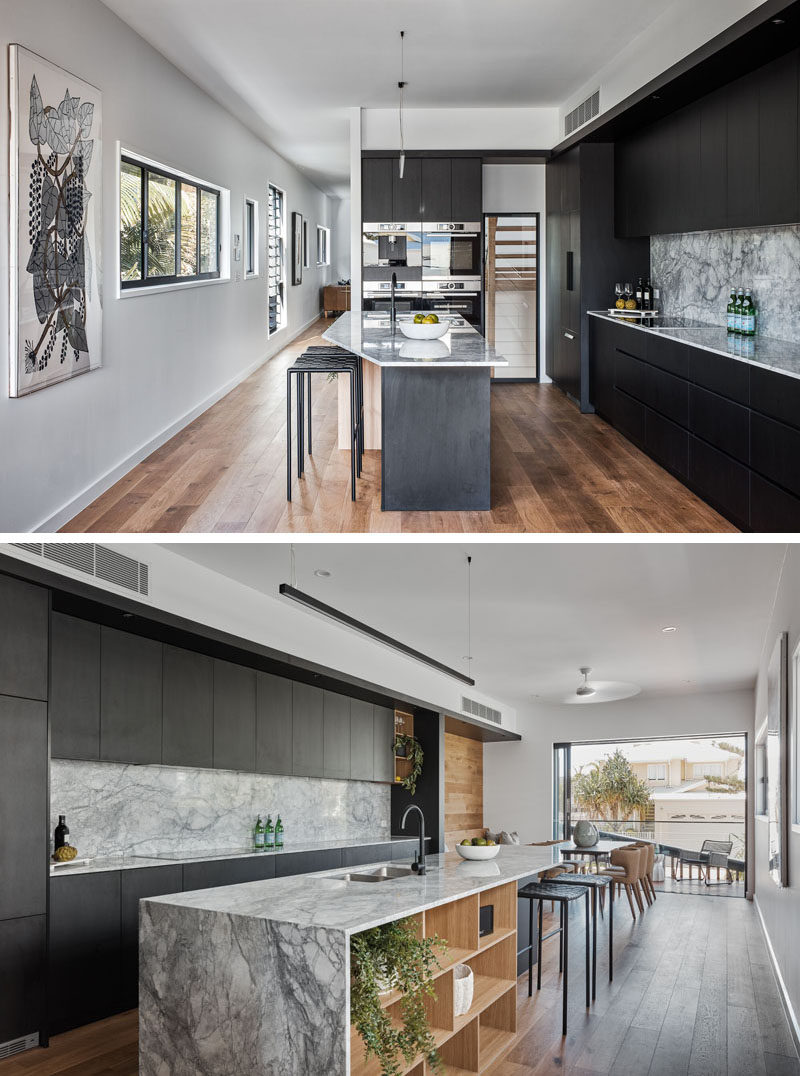 This modern kitchen features black cabinetry and an island with open shelving and seating on one side. #ModernKitchen #BlackKitchen #BlackCabinets