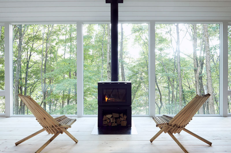 This modern cabin features black fireplace in front of large windows with tree views. #Fireplace #Windows #ModernCabin