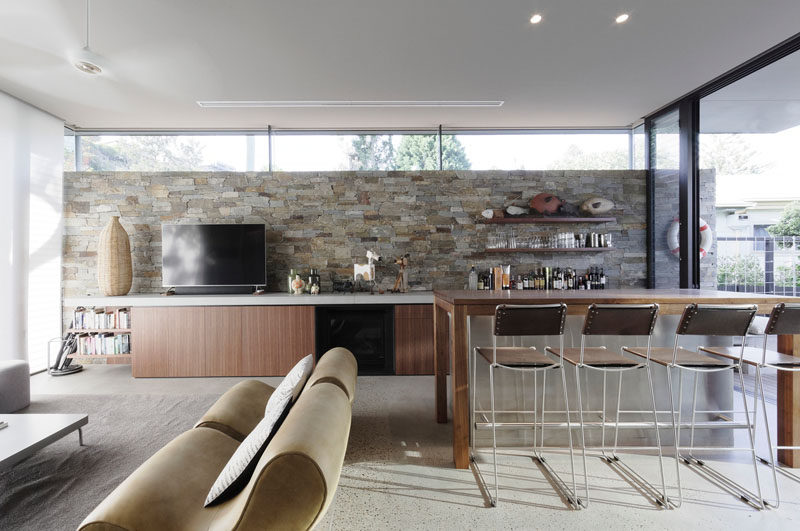 This modern games room has a stone wall, a bar that sits adjacent to a lounge, and sliding doors that open to an outdoor space. #GamesRoom #StoneWall #Bar