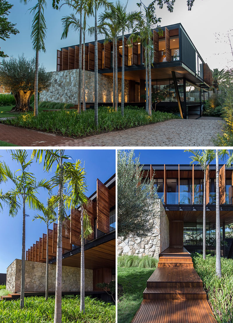 At the front of the multi-storey house, a wood path leading to the front door is surrounded by lush landscaping on one side, and a lawn with a single tree on the other. #ModernHouse #HouseDesign #ModernArchitecture #Landscaping