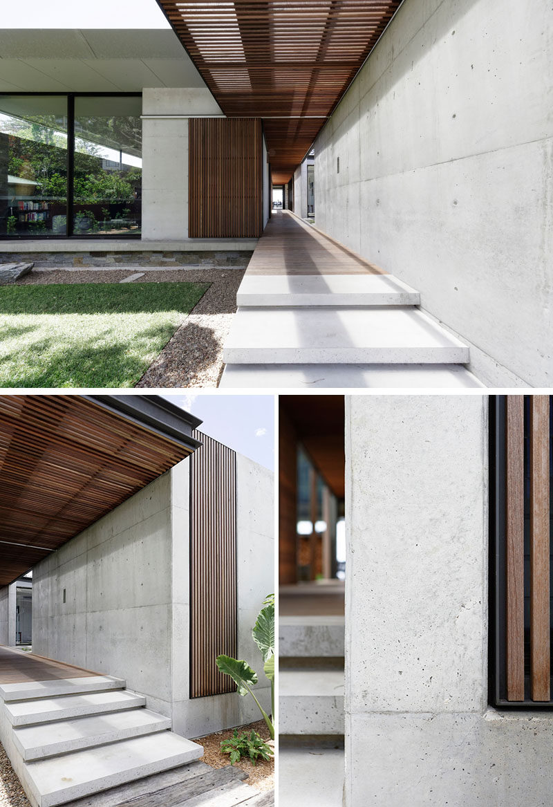 Concrete stairs alongside a concrete wall, lead to the sliding wood slat front door, that complements the breezeway that runs throughout this modern house. #WoodSlats #FrontDoor