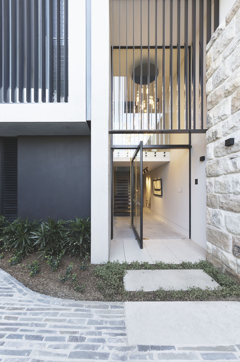 A large pivoting glass front door welcomes visitors to this modern house. #FrontDoor #PivotingDoor #GlassFrontDoor