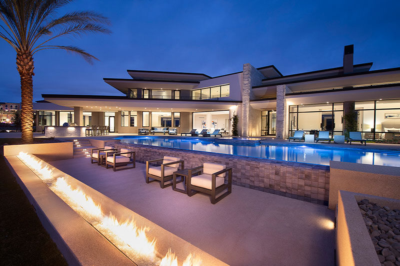 This modern house has an expansive outdoor entertaining space with a raised four-sided negative edge spa and a 37-foot-wide negative edge pool, as well as a low section of wall that features a built-in flame. #SwimmingPool #OutdoorFireplace #ModernHouse