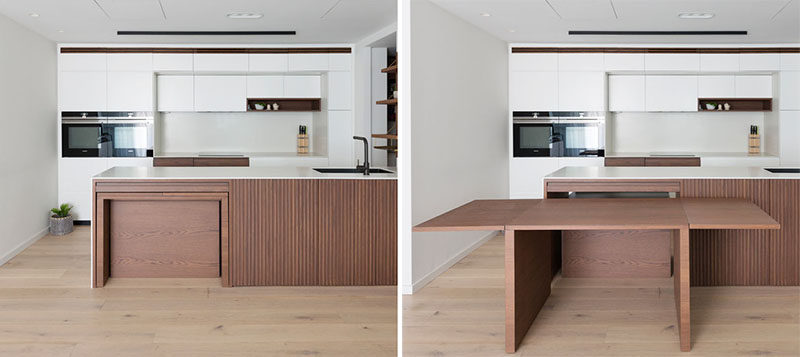 This modern kitchen features custom stained American Oak, corian countertops, and pull-out dining table, which sits flush within the kitchen bench and extends into a large dining table. #ModernKitchen #HiddenDiningTable #BuiltInDiningTable