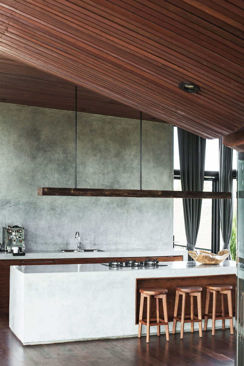 In this modern kitchen, glossy light colored countertops contrast the wood ceiling, floor, and accents, as well as the concrete wall. #Kitchen #KitchenDesign