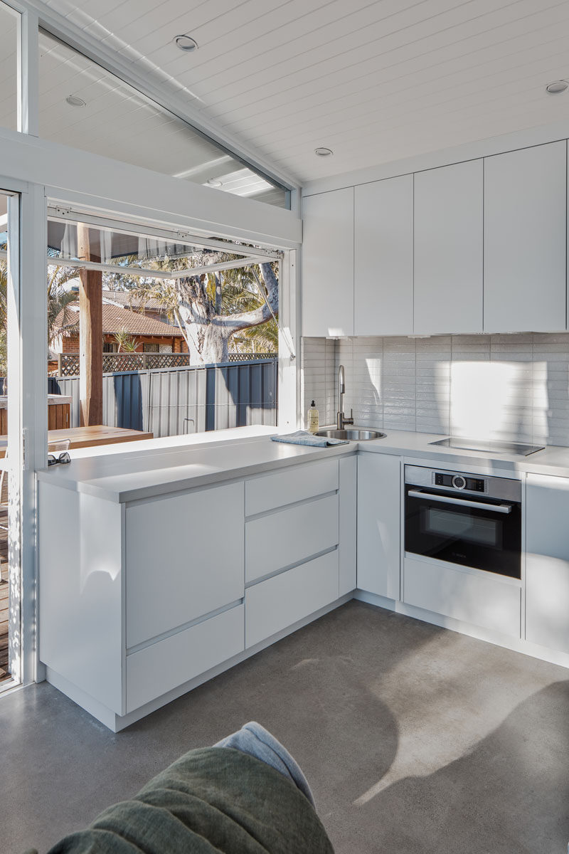 This small and bright kitchen has minimalist hardware free cabinets, a white tile backsplash, and complementing white countertop. #SmallKitchen #WhiteKitchen #ModernKitchen