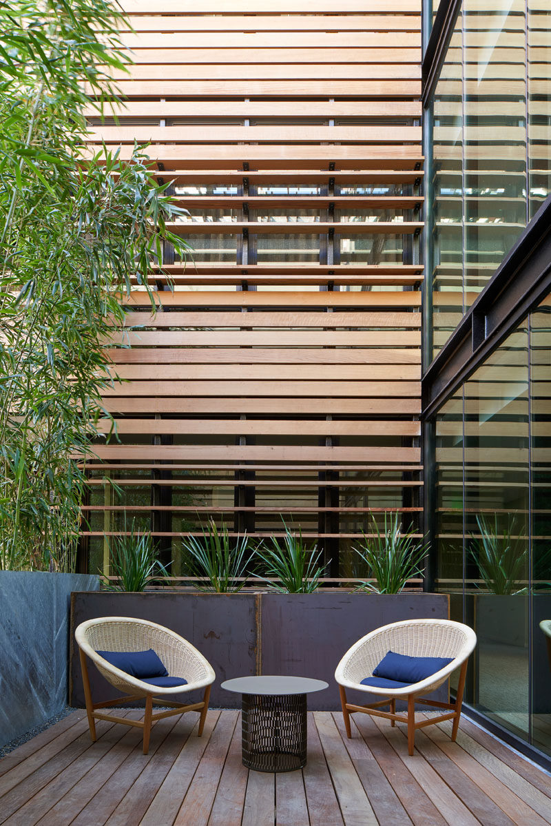 This modern hotel has a small seating area for two that's surrounded by glass, wood, and plants. #HotelDesign #OutdoorSpace