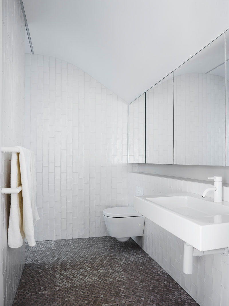 In this bathroom, penny tiles cover the floor while white subway tiles, laid vertically, cover the walls, and the mirrors reflect the light and curve in the ceiling. #ModernBathroom #BathroomDesign