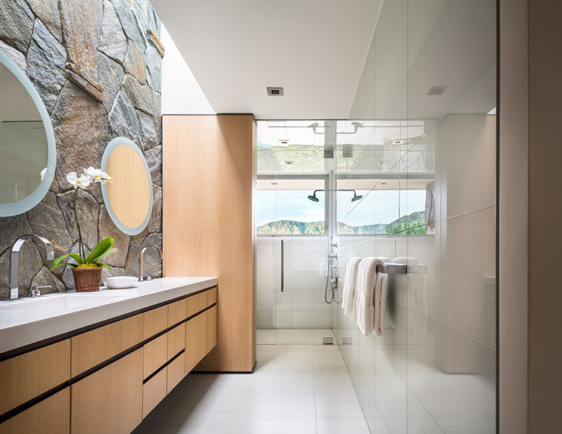 In this modern bathroom, a stone wall becomes the backdrop for the vanity, while a horizontal window in the shower allows natural light into the room. #StoneWall #ModernBathroom