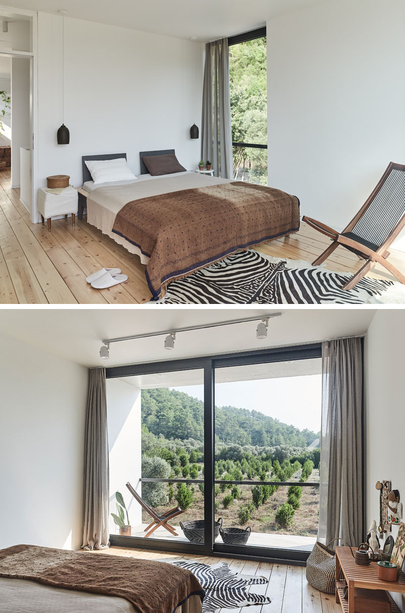 In this modern bedroom, simple matte black pendant lights hang from the ceiling and contrast the white walls. At the end of the bed is a sliding door that opens to a balcony overlooking the garden. #ModernBedroom #Balcony