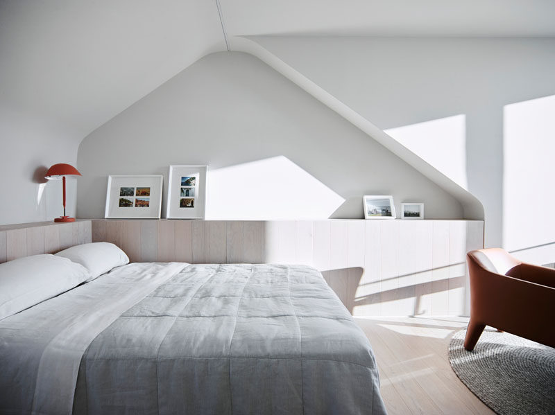 In this modern bedroom, large windows provide natural sunlight to filter through, while a cabinet lines the wall beneath a curved alcove. #ModernBedroom #BedroomDesign