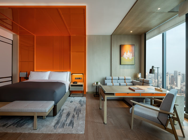 This modern hotel room features a bright orange headboard with hidden lighting, that wraps from behind the bed, up the wall, and onto the ceiling, creating a bold and colorful detail in the room that assists in making the room feel larger by drawing the eye upwards to the ceiling. #WrapAroundHeadboard #Headboard #Bedroom