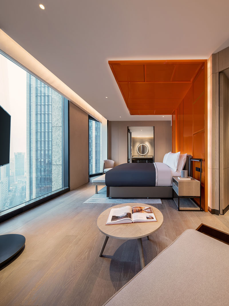 This modern hotel room features a bright orange headboard with hidden lighting, that wraps from behind the bed, up the wall, and onto the ceiling, creating a bold and colorful detail in the room that assists in making the room feel larger by drawing the eye upwards to the ceiling. #WrapAroundHeadboard #Headboard #Bedroom