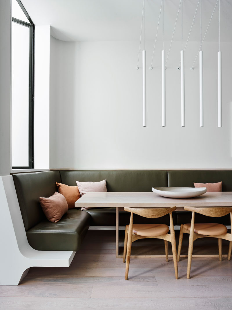 This modern dining area with minimalist white pendant lights, also features built-in seating in the form of a banquette that wraps around the corner. #DiningRoom #Banquette