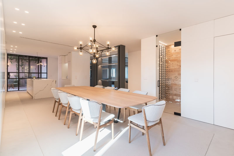 In this modern dining room, a sculptural black chandelier hangs above a large wood dining table, that's surrounded by light grey upholstered dining chairs. #ModernDiningRoom #DiningRoom