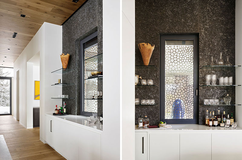 Adjacent to the kitchen in this modern guesthouse, is a bar area that highlights the metal screen outside, and makes use of glass shelving to display a variety of glassware. #Bar #HomeBar #Shelving