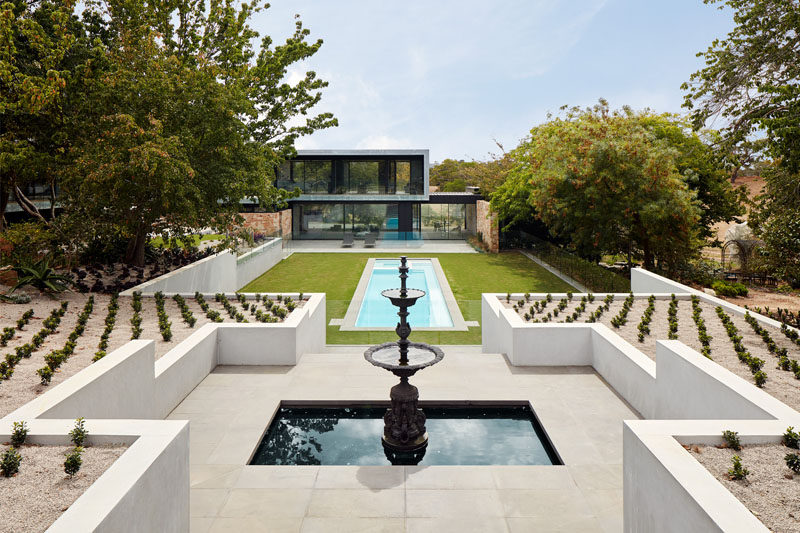 At the end of the pool are stairs that lead up to a fountain, while on either side of the fountain are perfectly arranged plants in a symmetrical pattern. #Landscaping #SwimmingPool #Fountain #Garden