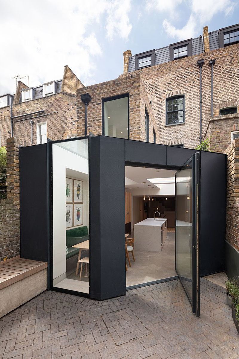 A large black-framed pivoting glass door connects the dining room and kitchen within this extension to the rear garden. #RearExtension #PivotingDoor