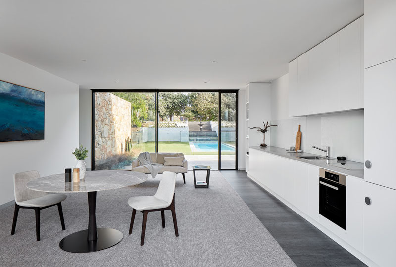 This modern home has a guest suite on the lower level of the house that features a kitchen that runs along the wall, and a view of the pool and a fountain in the distance. #GuestSuite #WhiteKitchen #MinimalistKitchen