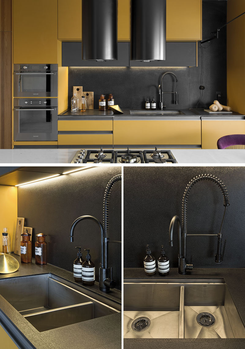 This modern kitchen has been named the 'Dijon Kitchen' due to the mustard cabinet color, while black accents like the backsplash, countertop, and faucet, complement the support structures of the island. #UndermountSink #KitchenDesign #ModernKitchen