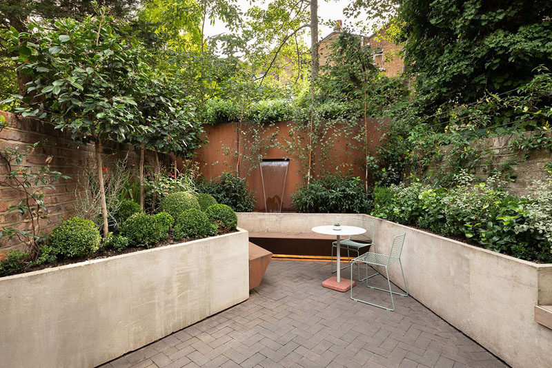 In this modern garden, custom-designed planters wrap around the patio, helping to create depth, while a small seating area and water feature are the focal point of the outdoor space. #ModernGarden #GardenDesign #Landscaping #LandscapeDesign