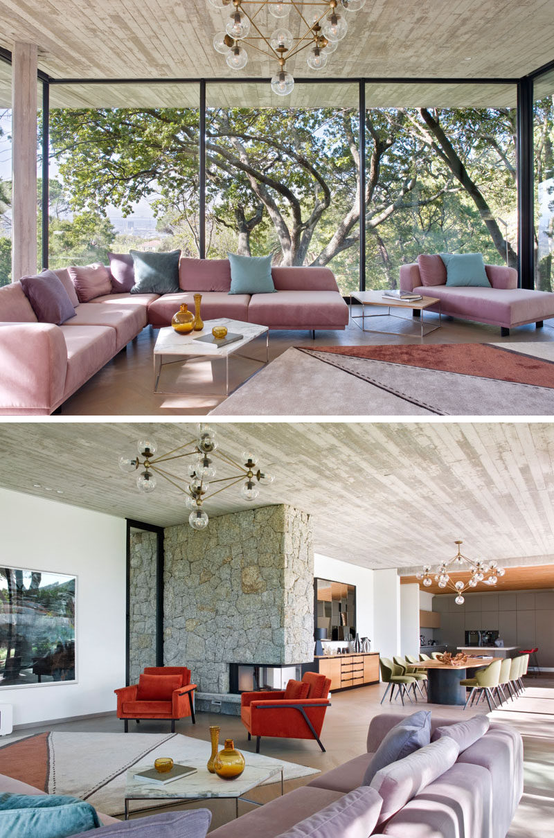 Inside this modern house, floor-to-ceiling windows provide a natural backdrop for the living room that features an L-shaped sofa with chaise, as well a pair of customized Maxx armchairs. A see-through fireplace has been embedded within a surround of rough-hewn granite. #ModernLivingRoom #ModernWindows #Fireplace