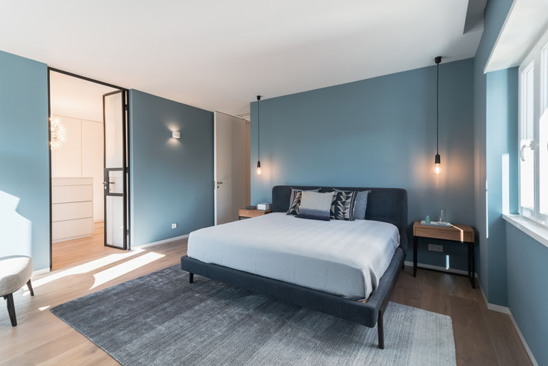 In this modern master bedroom, the designers decided to paint the walls in a sophisticated blue, to provide a special contrast from the other spaces in the apartment. #BlueBedroom #BedroomDesign #ModernBedroom