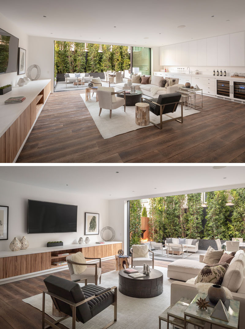 This modern and oversized great room features floor-to-ceiling windows that open to provide access to a patio. Red Gum was selected as an accenting wood on the first floor, and is used on the cabinetry that runs along the wall. #GreatRoom #ModernInterior #LivingRoom