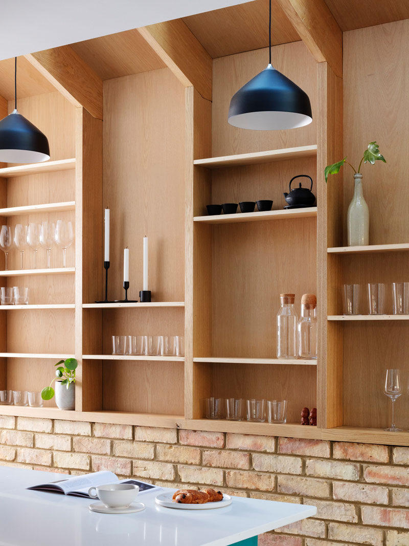 Running along the wall in this house, is a custom-designed wood wall pantry, with shelving and black pendant lights. #WallPantry #Pantry #InteriorDesign