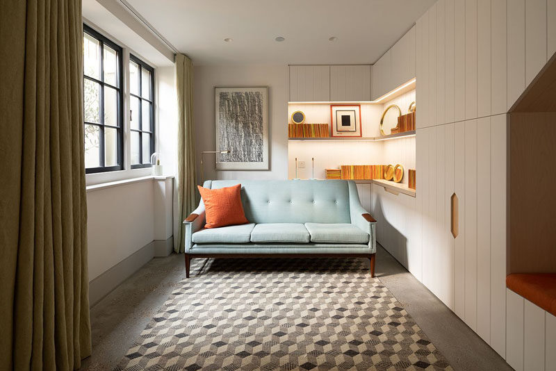 This small sitting room has custom cabinetry that wraps around the room to provide storage, and open shelving allows for displaying personal items. #SittingRoom #Cabinetry #Shelving