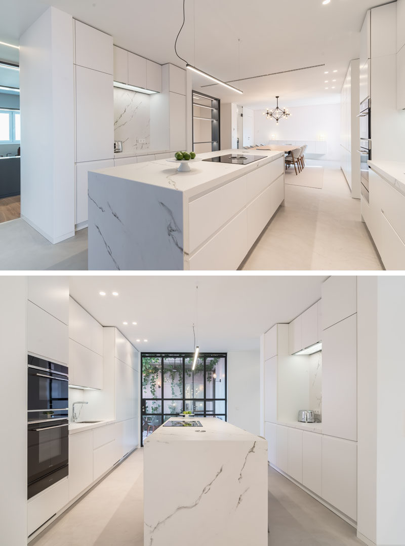 In this modern kitchen, minimalist white cabinets line the walls and a large island is centrally located. #ModernWhiteKitchen #ModernKitchen #WhiteKitchen