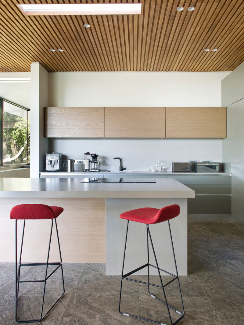 In this modern kitchen, a wood slat ceiling helps to define the space, while Etch bar stools in clementine orange add a pop of color to the mostly neutral palette. #ModernKitchen #KitchenDesign