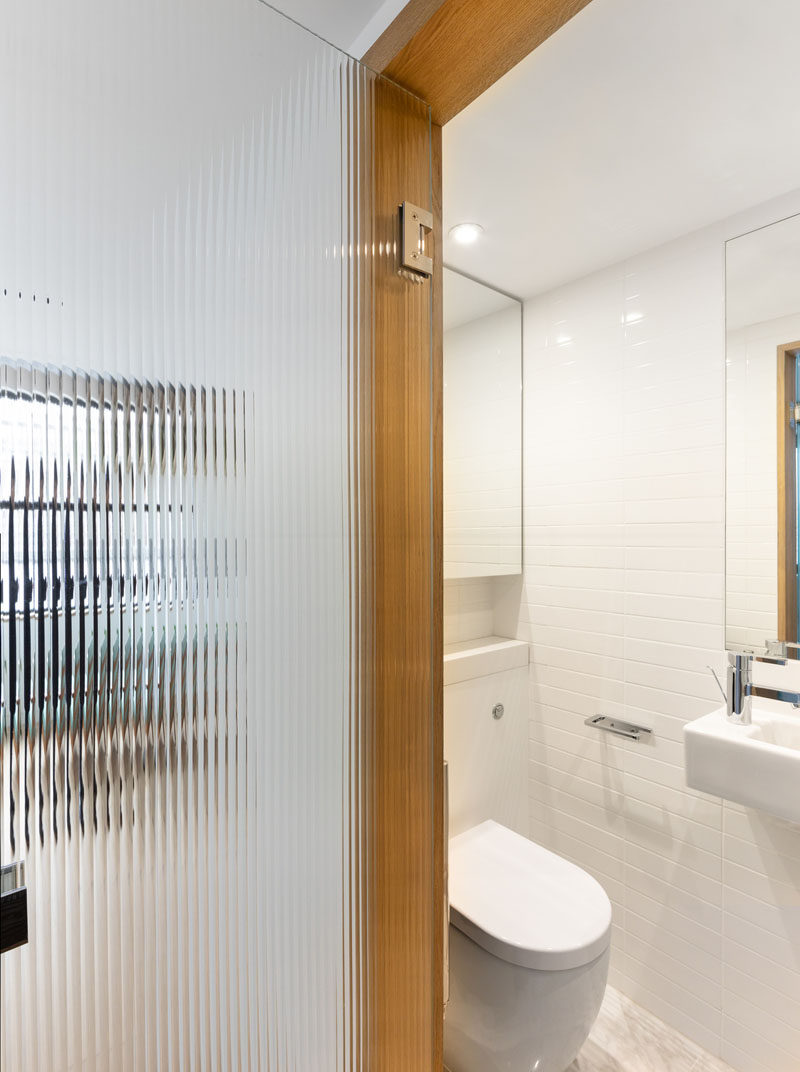 This small modern bathroom has white tiled walls, while a textured glass door allows natural light to pass through to the interior. #SmallBathroom #BathroomDesign