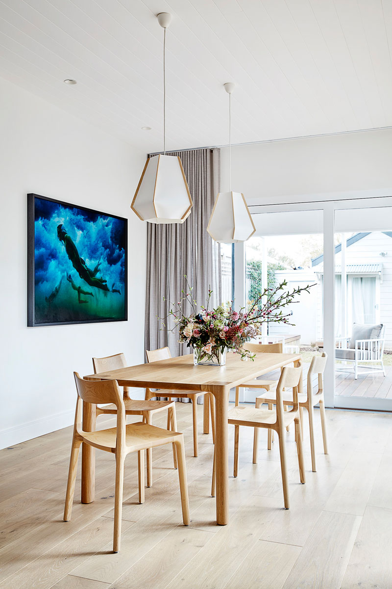 In this modern dining room, two geometric pendant lights hang above a wood dining table and its chairs, while art adds color to the white walls and ceiling. #DiningRoom #ModernDiningRoom #DiningRoomIdeas